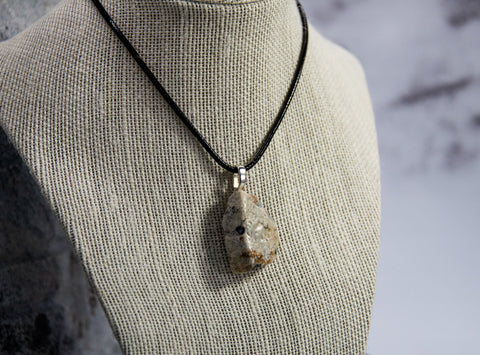 A dramatic example of a Canadian Shield rock. White Quartz marked throughout with accents and intrusions in white, red and black, on a woven black leather cord (12 in, 31 cm)